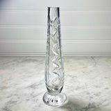 A clear cut-crystal vase with a spiral diamond pattern, standing on a round base against a white paneled wall and marble surface.