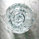 Vintage Zawiercie Laurencie Cut Glass Tall Crystal Cracker Jar viewed from directly above, featuring intricate geometric facets and a central floral pattern, set against a light gray marble background.