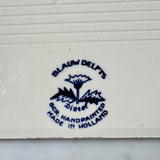 Blue Blauw Delfts Distel logo and text on a white background on back of tile