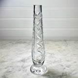 A clear cut-crystal vase with a spiral diamond pattern, standing on a round base against a white paneled wall and marble surface.
